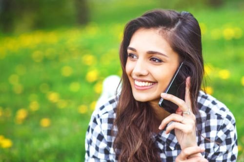 callfrd speaking image Portrait of a beautiful woman typing on the smart phone in a park with a green unfocused background. Hipster woman texting in summer